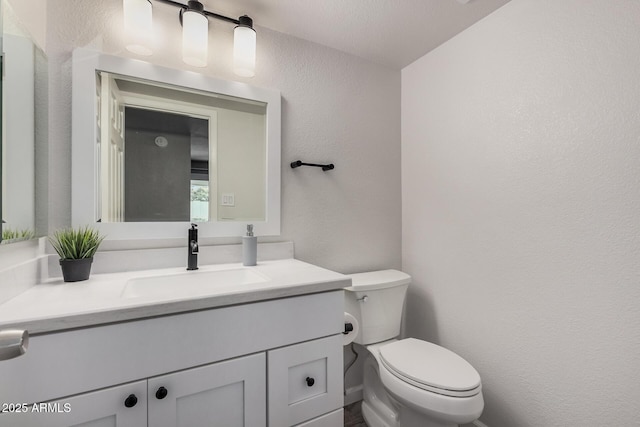 half bath with toilet, vanity, and a textured wall