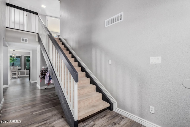 stairway featuring visible vents, a towering ceiling, baseboards, and wood finished floors