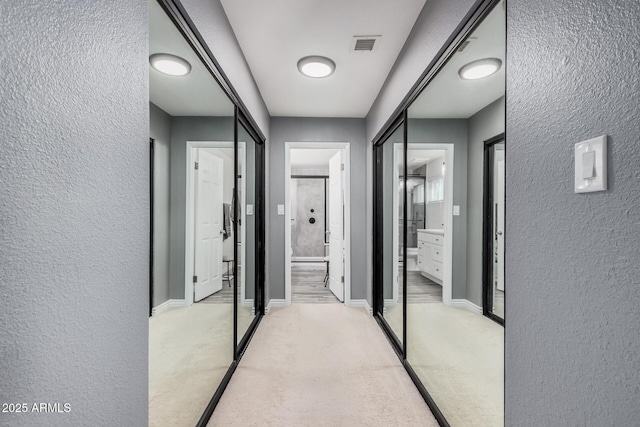 hallway featuring light colored carpet, visible vents, and a textured wall