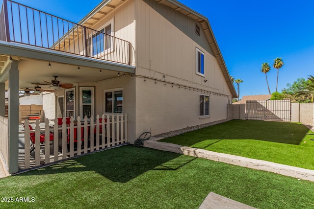 view of side of property featuring a balcony, ceiling fan, fence private yard, a patio area, and a lawn