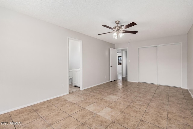 unfurnished bedroom featuring a closet, light tile patterned floors, baseboards, ensuite bathroom, and a textured ceiling