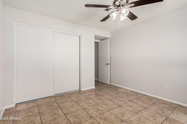 unfurnished bedroom featuring a textured ceiling, a closet, light tile patterned floors, and baseboards