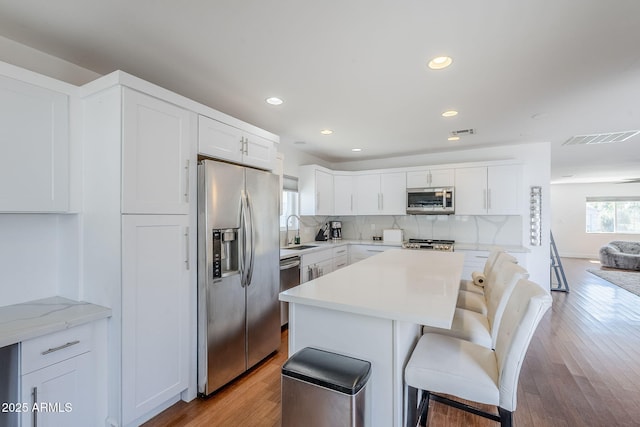 kitchen with visible vents, a breakfast bar area, decorative backsplash, appliances with stainless steel finishes, and a sink