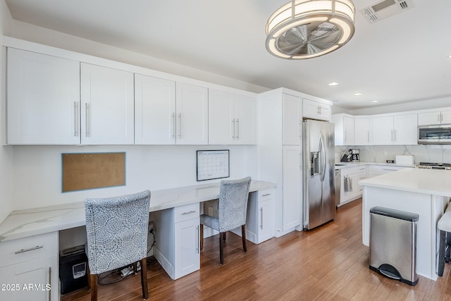 interior space with wood finished floors, recessed lighting, visible vents, and built in desk