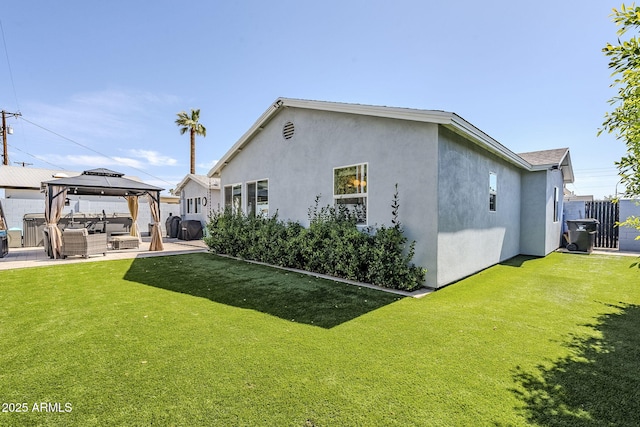 rear view of property featuring fence, a yard, stucco siding, a gazebo, and a patio area