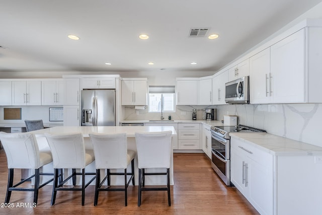 kitchen featuring a kitchen bar, visible vents, a center island, stainless steel appliances, and white cabinets