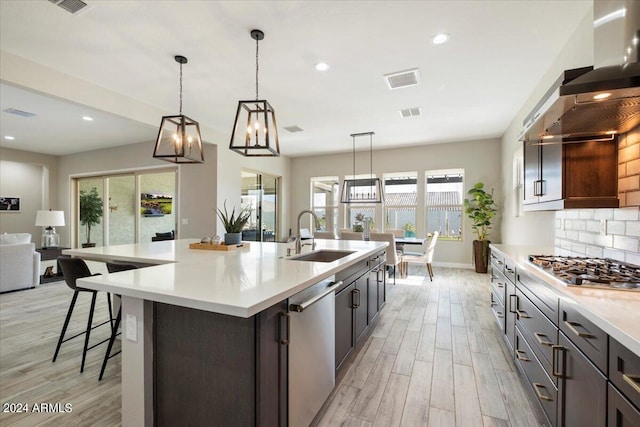 kitchen with tasteful backsplash, hanging light fixtures, sink, stainless steel appliances, and a center island with sink