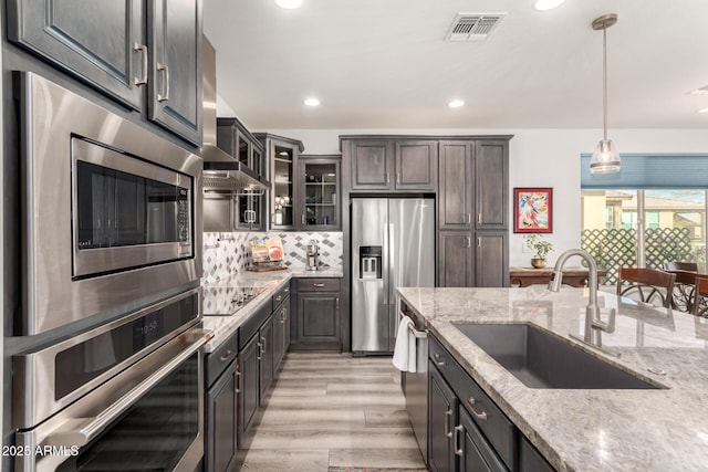 kitchen with pendant lighting, light stone countertops, stainless steel appliances, and sink