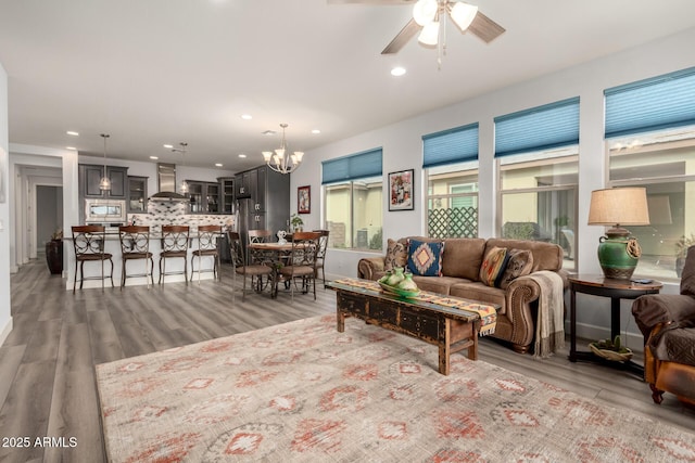 living room featuring ceiling fan with notable chandelier and light wood-type flooring