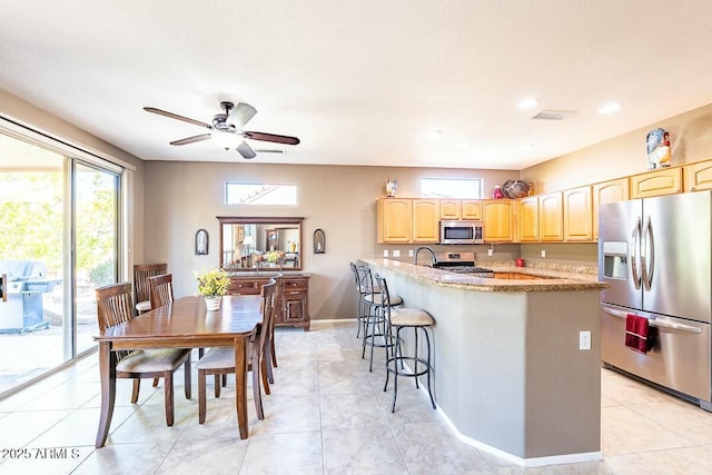 kitchen with ceiling fan, stainless steel appliances, light stone counters, a breakfast bar, and light tile patterned floors