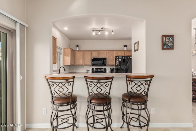 kitchen with a peninsula, black appliances, a kitchen breakfast bar, and light countertops