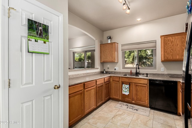 kitchen with arched walkways, brown cabinets, rail lighting, a sink, and dishwasher