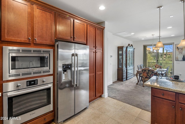 kitchen with appliances with stainless steel finishes, light colored carpet, light stone counters, and decorative light fixtures