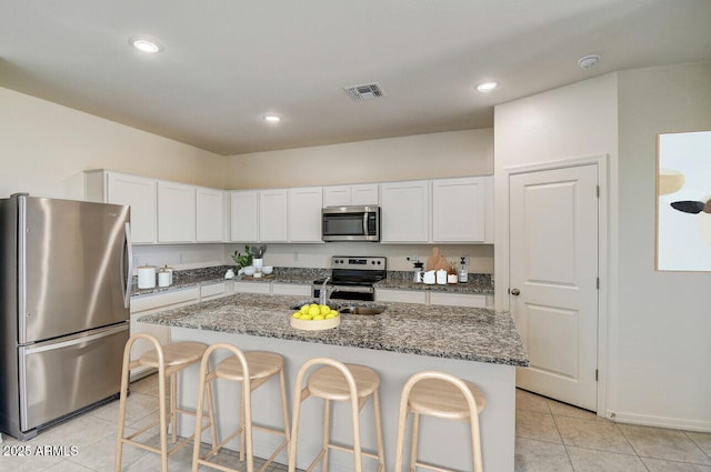 kitchen with a kitchen bar, white cabinetry, dark stone countertops, stainless steel appliances, and a kitchen island with sink