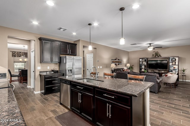 kitchen with appliances with stainless steel finishes, dark stone counters, ceiling fan, sink, and hanging light fixtures