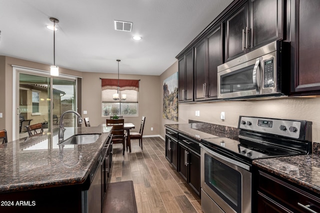 kitchen with pendant lighting, a kitchen island with sink, an inviting chandelier, sink, and appliances with stainless steel finishes