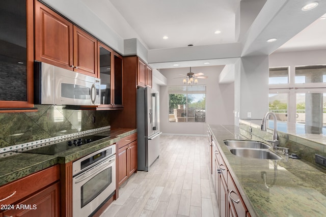 kitchen with light wood-type flooring, backsplash, light stone counters, stainless steel appliances, and sink