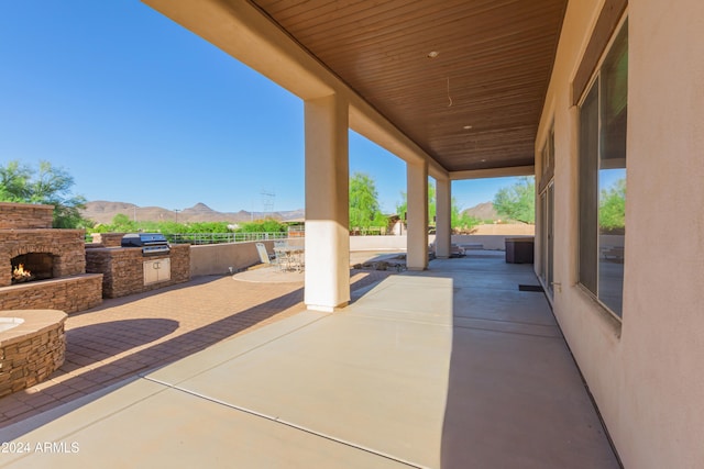 view of patio / terrace featuring a mountain view, exterior kitchen, and an outdoor stone fireplace