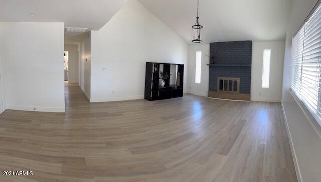 unfurnished living room with high vaulted ceiling, light hardwood / wood-style floors, and a brick fireplace