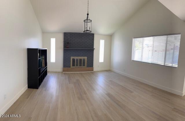 unfurnished living room with light wood-type flooring, high vaulted ceiling, and a brick fireplace