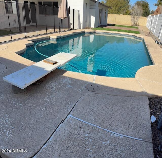 view of swimming pool featuring a patio and a diving board