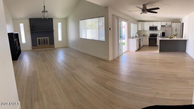 unfurnished living room with lofted ceiling, sink, a brick fireplace, ceiling fan, and light hardwood / wood-style floors