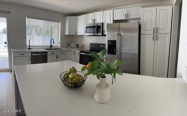 kitchen featuring light stone counters, sink, white cabinets, and black appliances