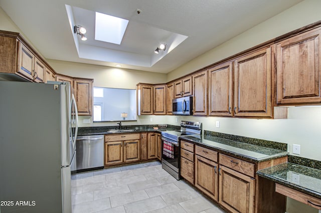 kitchen with dark stone countertops, sink, a skylight, stainless steel appliances, and a raised ceiling