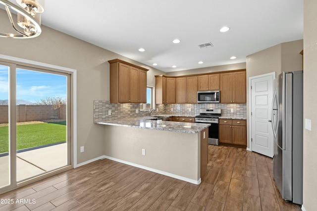 kitchen with pendant lighting, sink, decorative backsplash, appliances with stainless steel finishes, and kitchen peninsula