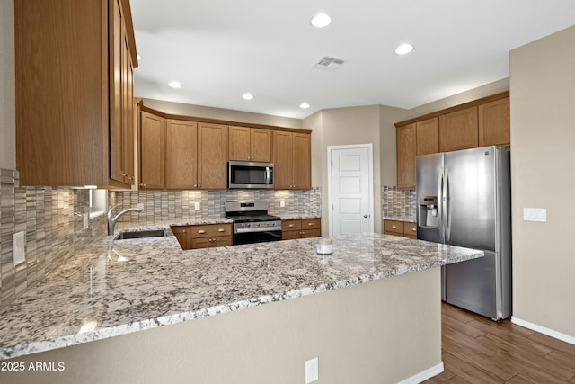 kitchen featuring kitchen peninsula, light stone countertops, sink, and stainless steel appliances