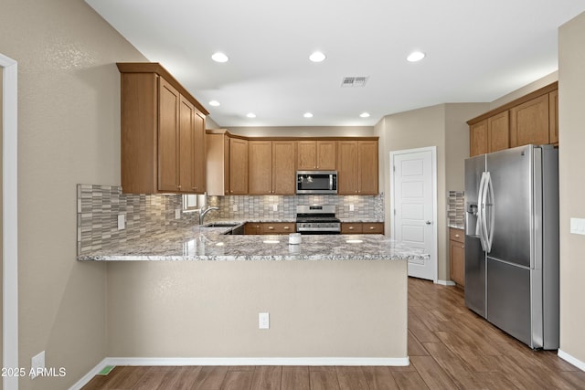 kitchen featuring kitchen peninsula, light stone countertops, backsplash, stainless steel appliances, and light hardwood / wood-style floors