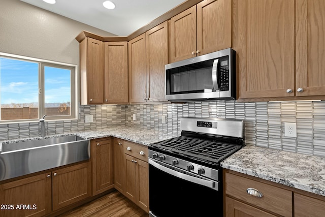 kitchen featuring sink, tasteful backsplash, light stone counters, light hardwood / wood-style floors, and appliances with stainless steel finishes