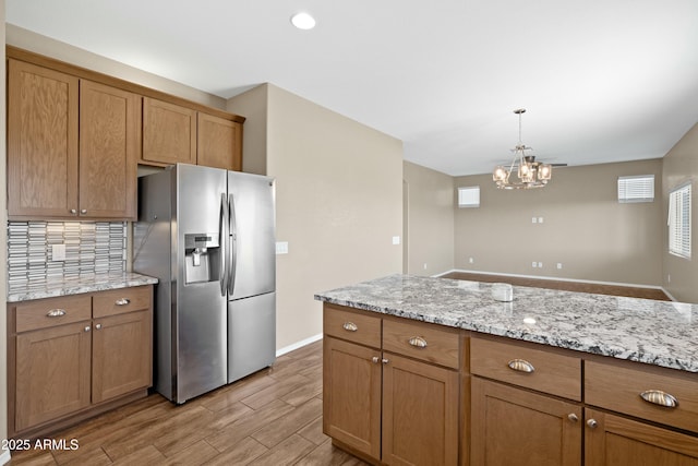 kitchen with tasteful backsplash, light stone counters, a chandelier, stainless steel fridge with ice dispenser, and hanging light fixtures