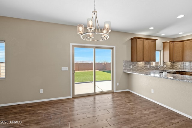 kitchen featuring tasteful backsplash, light stone counters, sink, pendant lighting, and a chandelier