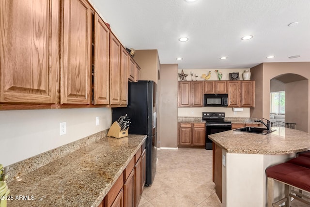 42160 W Arvada Ct, Maricopa, AZ 85138 - kitchen featuring black appliances, a sink, arched walkways, brown cabinetry, and a kitchen bar