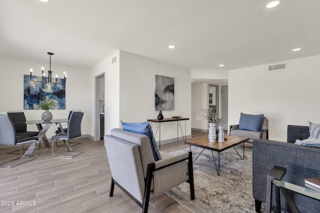 living room with an inviting chandelier, light wood-style flooring, and visible vents