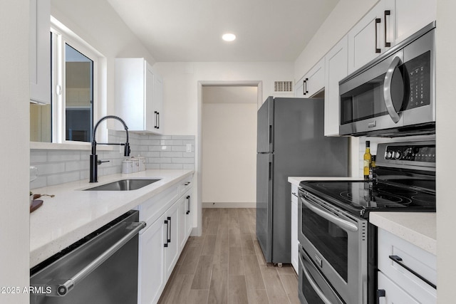 kitchen with tasteful backsplash, appliances with stainless steel finishes, white cabinets, a sink, and visible vents