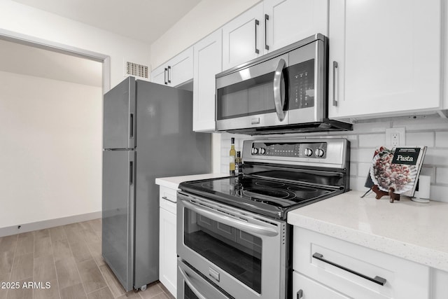 kitchen with light stone counters, stainless steel appliances, white cabinets, light wood-type flooring, and visible vents