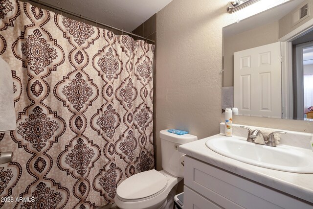 bathroom with vanity, visible vents, toilet, curtained shower, and a textured wall