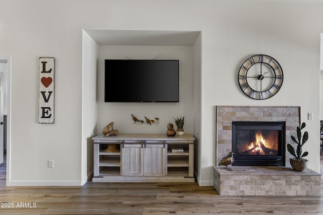 interior space with a lit fireplace, wood finished floors, and baseboards