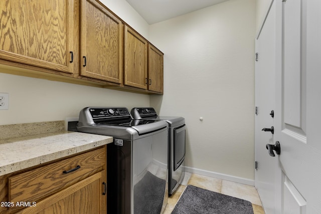 clothes washing area with light tile patterned floors, separate washer and dryer, cabinet space, and baseboards