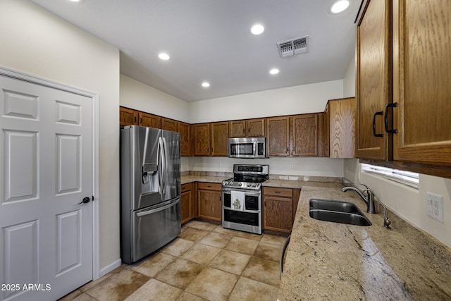 kitchen with a sink, visible vents, appliances with stainless steel finishes, light stone countertops, and brown cabinetry