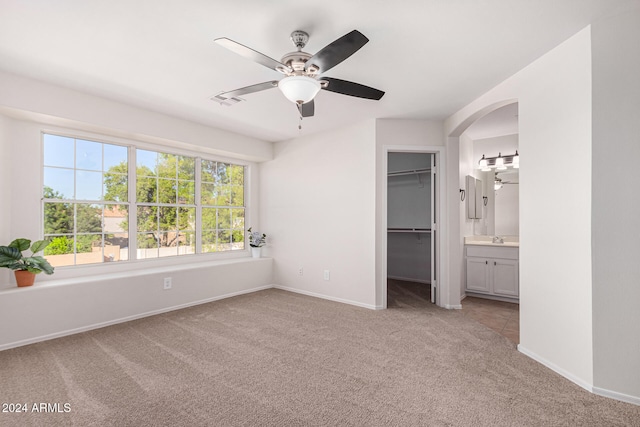 unfurnished bedroom with sink, a walk in closet, ensuite bath, ceiling fan, and light colored carpet