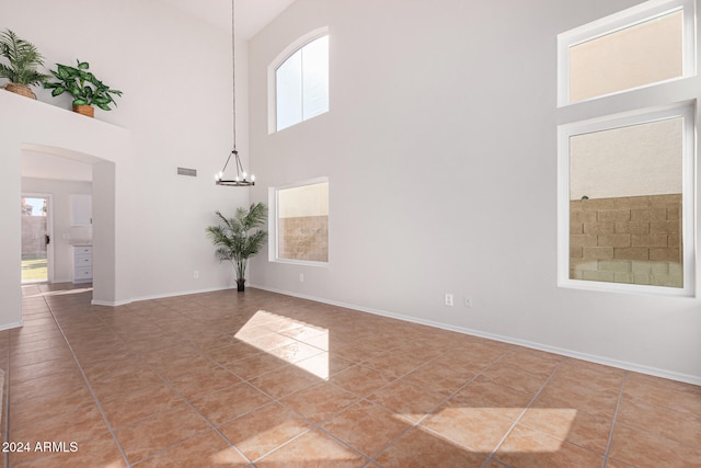 tiled spare room featuring a notable chandelier, a towering ceiling, and a wealth of natural light