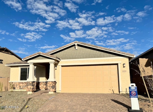 view of front of house featuring decorative driveway, stone siding, an attached garage, and stucco siding