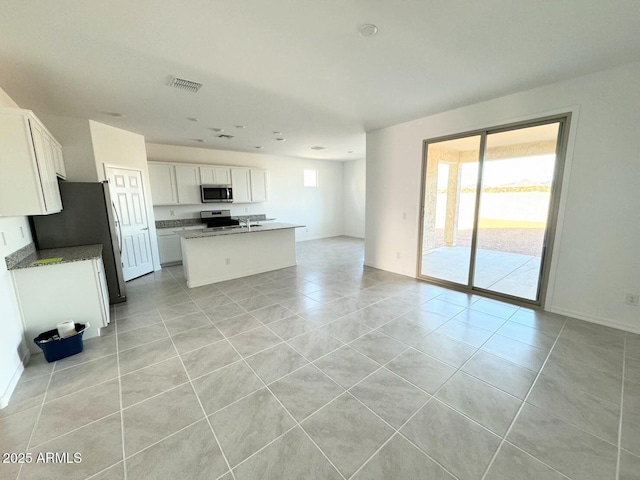 kitchen featuring open floor plan, appliances with stainless steel finishes, light tile patterned flooring, white cabinetry, and a kitchen island with sink