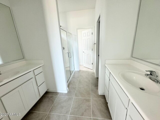 bathroom with tile patterned floors, a stall shower, two vanities, and a sink