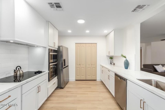 kitchen featuring backsplash, light wood-type flooring, appliances with stainless steel finishes, light stone counters, and white cabinetry