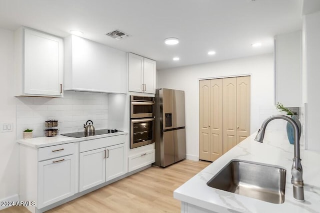 kitchen with sink, light stone counters, light hardwood / wood-style flooring, white cabinets, and appliances with stainless steel finishes