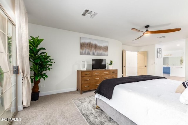 bedroom with ceiling fan, light colored carpet, and ensuite bath